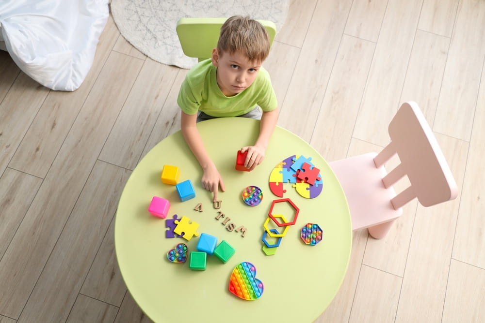 Little boy with word AUTISM and toys on table at home, top view
